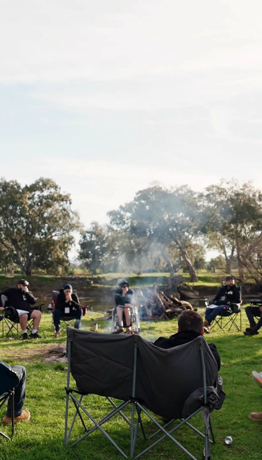 Camp chairs drawn into a circle around the fire beside the river