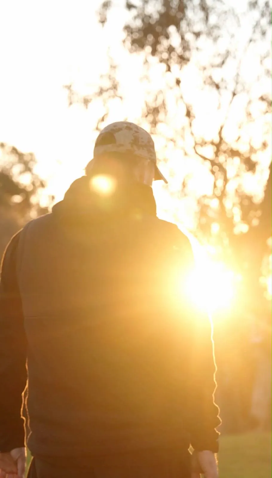 A man standing alone at sunrise, backlit by the sun through the gum trees